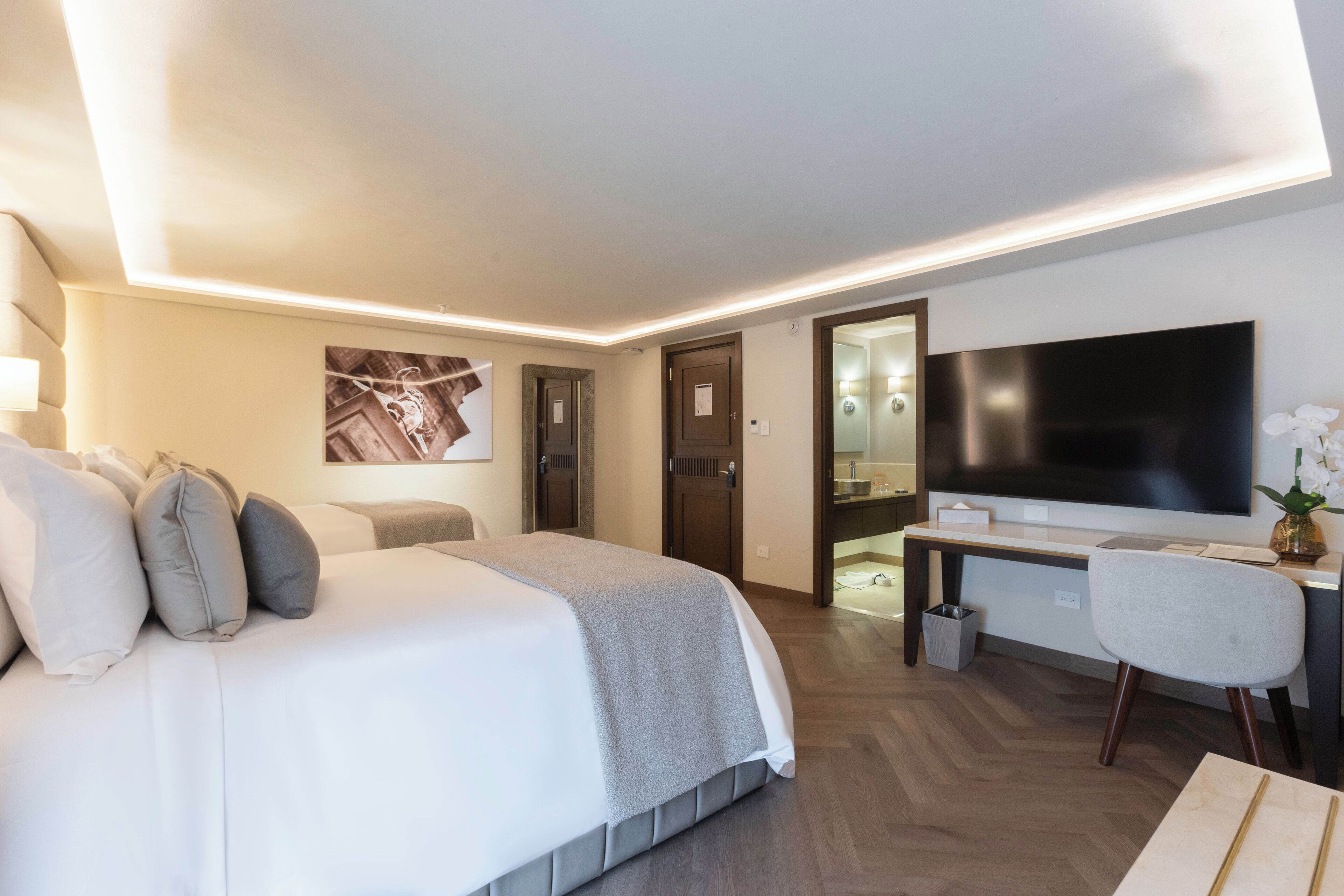 A modern hotel room with a large bed, a desk, a flat-screen TV, and a bathroom visible through an open door.