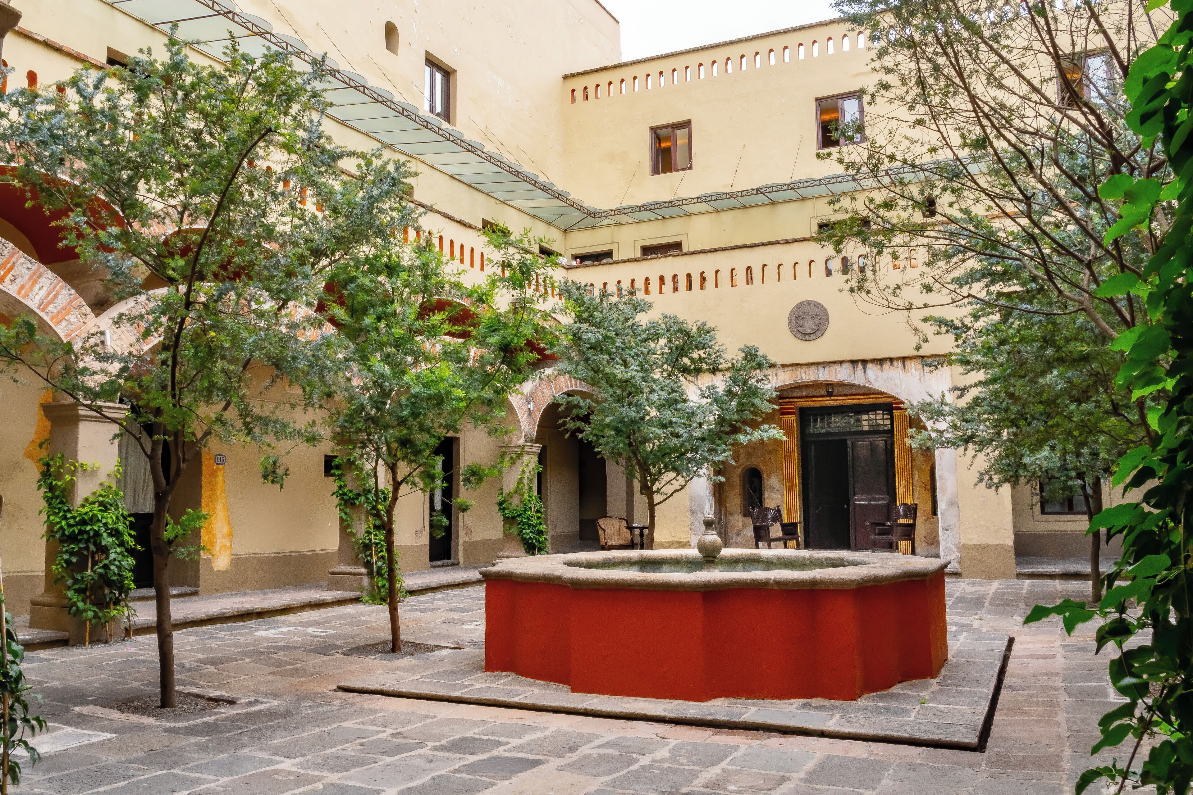 A courtyard with a central fountain, stone flooring, and surrounding trees.