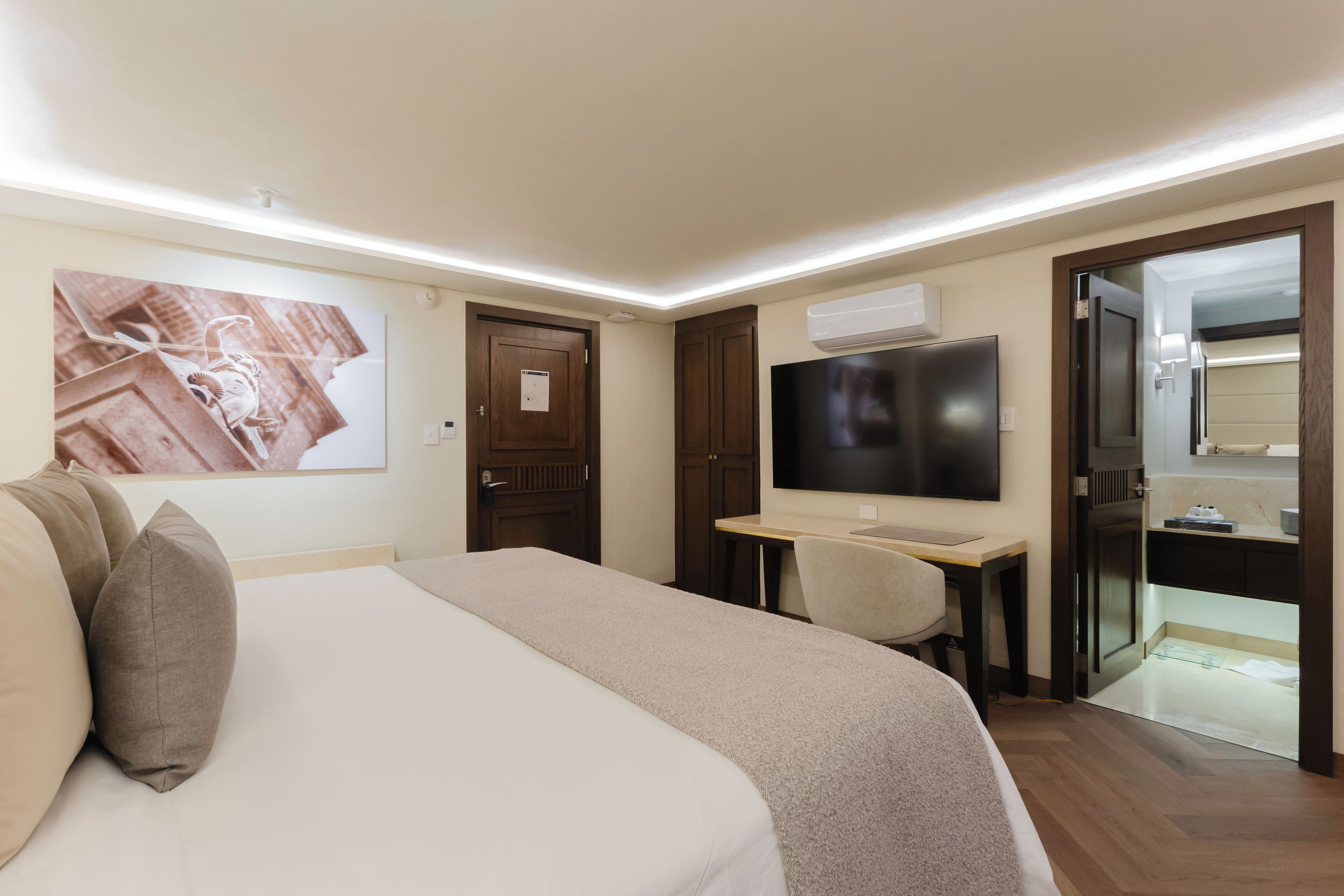 A hotel room with a bed, a desk, a television, and a door leading to a bathroom.