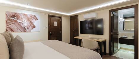 A hotel room with a bed, a desk, a television, and a door leading to a bathroom.