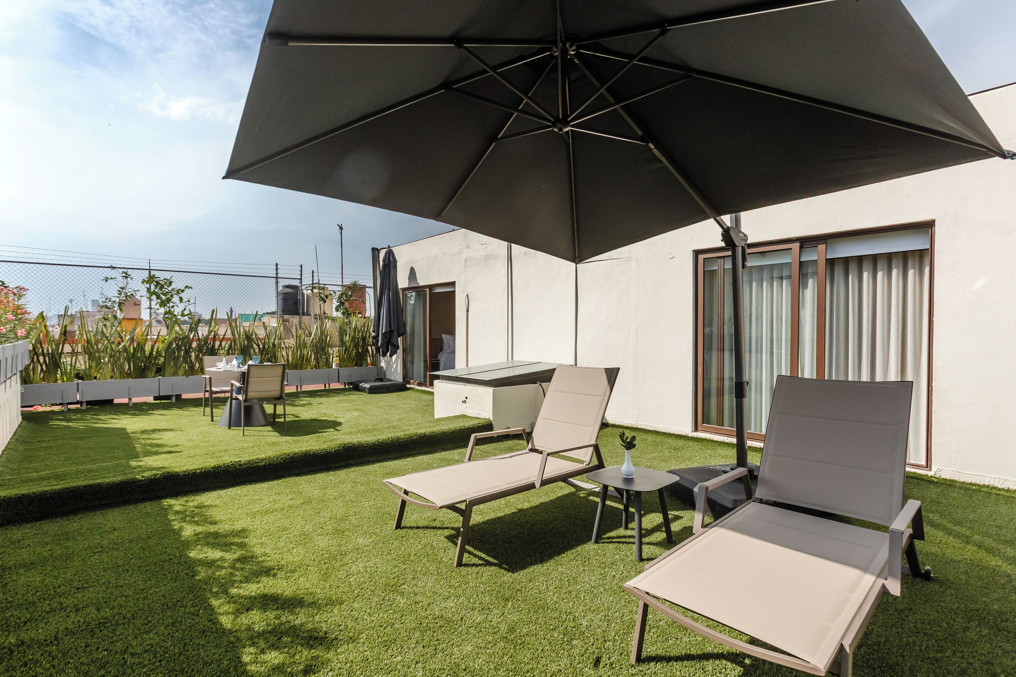 Una terraza en la azotea con césped artificial, dos sillones de relax, una mesa y un parasol grande.