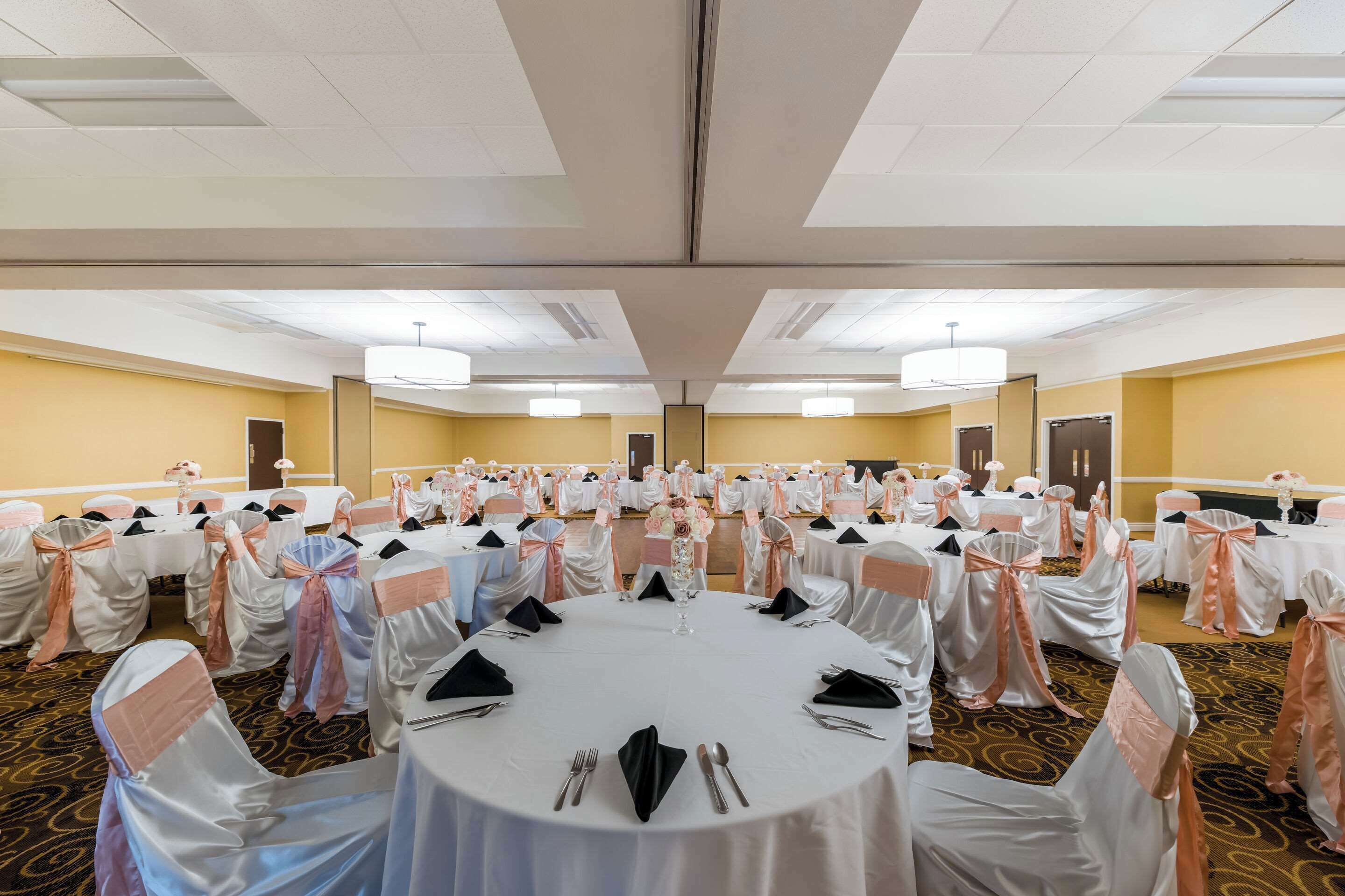 Une salle de banquet avec des tables rondes dressées pour un événement formel, agrémentée de nappes blanches et de chaises ornées de rubans roses.