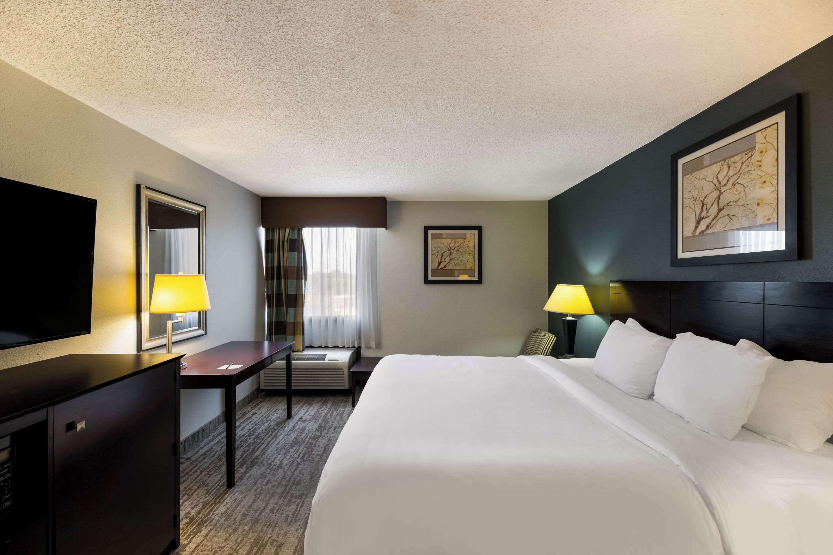 A hotel room with a large bed, a desk, a chair, a TV, and two lamps.
