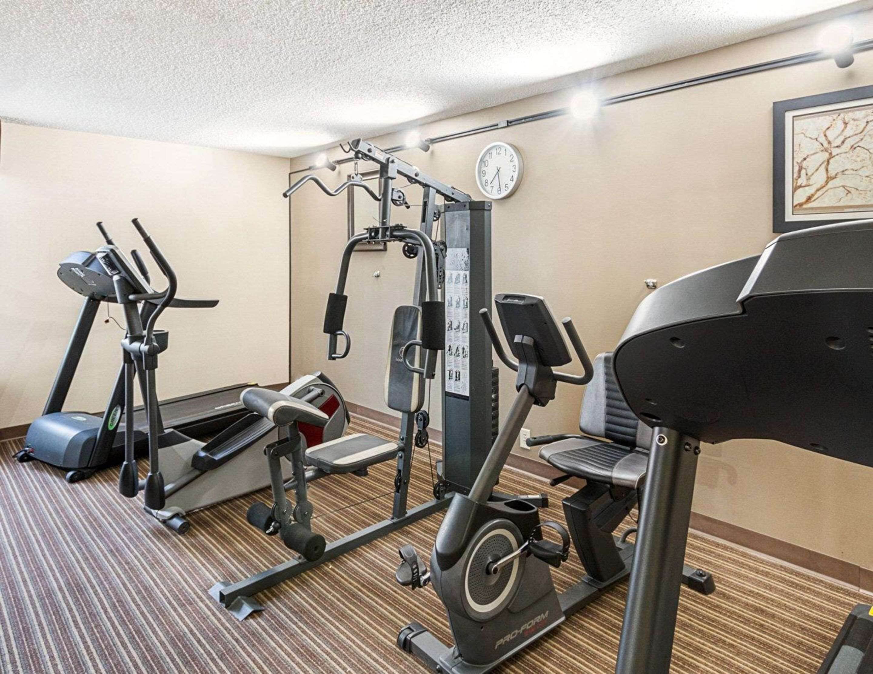 A hotel gym with cardio machines, weight training equipment, and a clock on the wall.