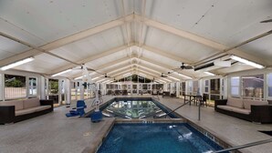 An indoor swimming pool with a clear view of the pool area, including the pool's edge, a diving board, and seating areas with sofas and chairs. - Clarion Hotel San Angelo near Convention Center (San Angelo)