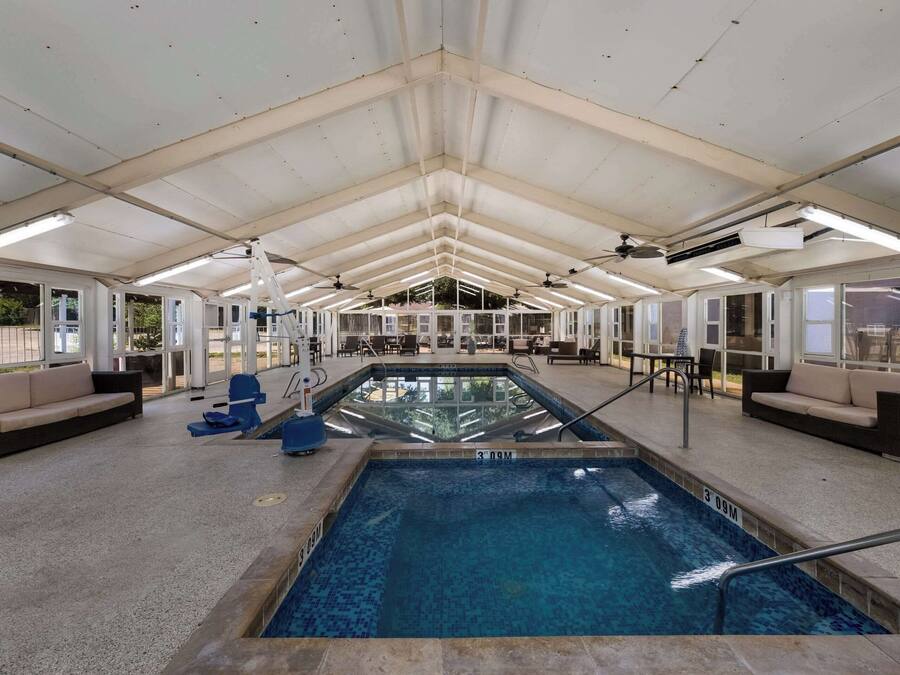 Una piscina interior con una vista clara del área de la piscina, incluyendo el borde de la piscina, un trampolín y zonas de estar con sofás y sillones.