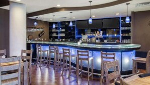 A bar area with wooden chairs and a counter, featuring a modern design with blue lighting and shelves stocked with bottles. - Clarion Hotel San Angelo near Convention Center (San Angelo)
