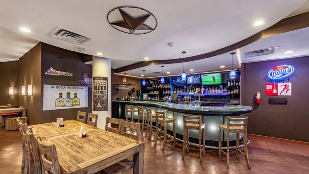 A bar area with a counter, bar stools, and a large screen displaying sports. - Clarion Hotel San Angelo near Convention Center (San Angelo)