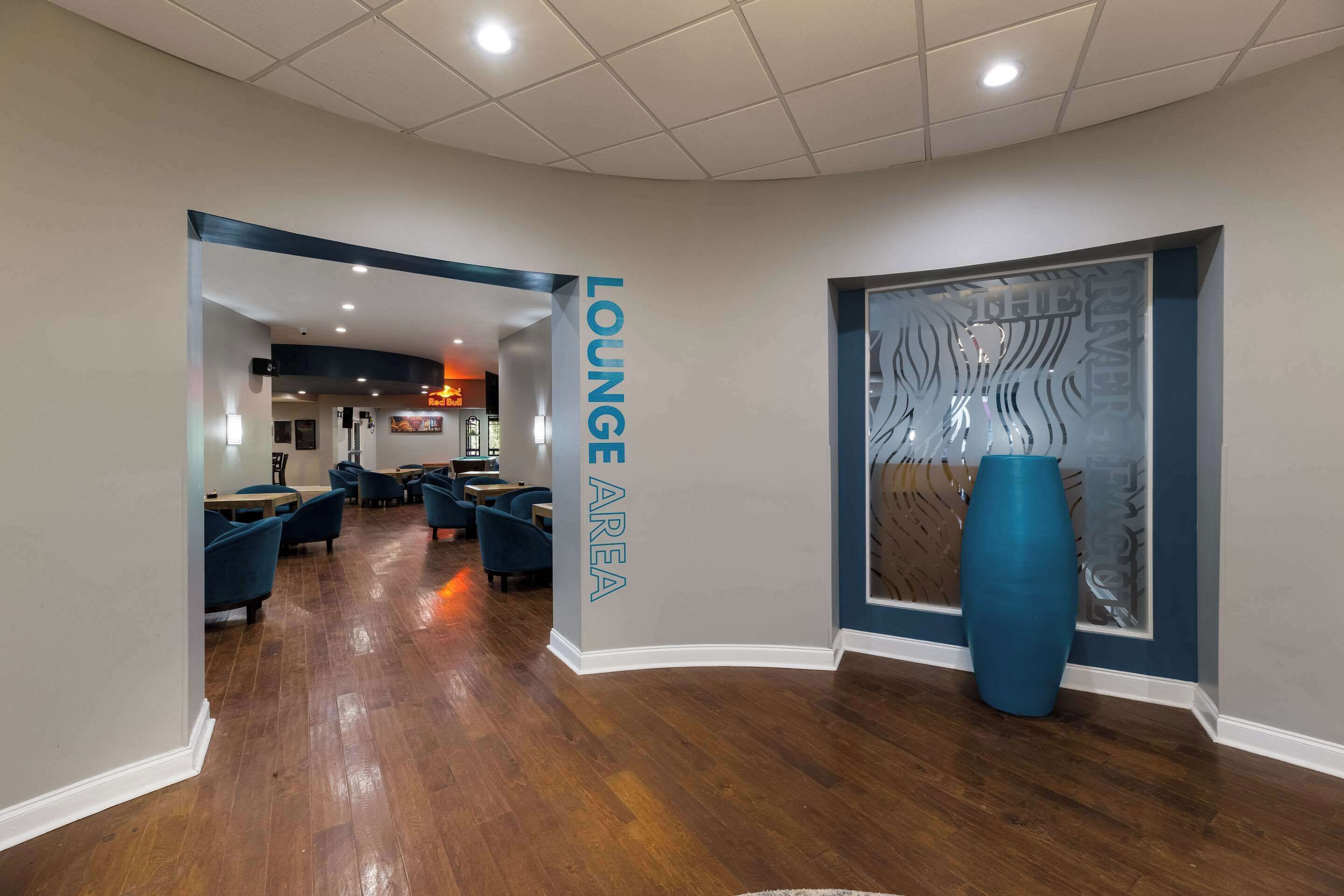 A lounge area with wooden flooring, blue chairs, and a large blue vase.