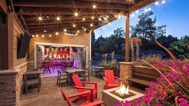 An outdoor patio with red Adirondack chairs, a fire pit, and a bar area with a view of the outdoors. - Hampton Inn Pullman (Pullman)