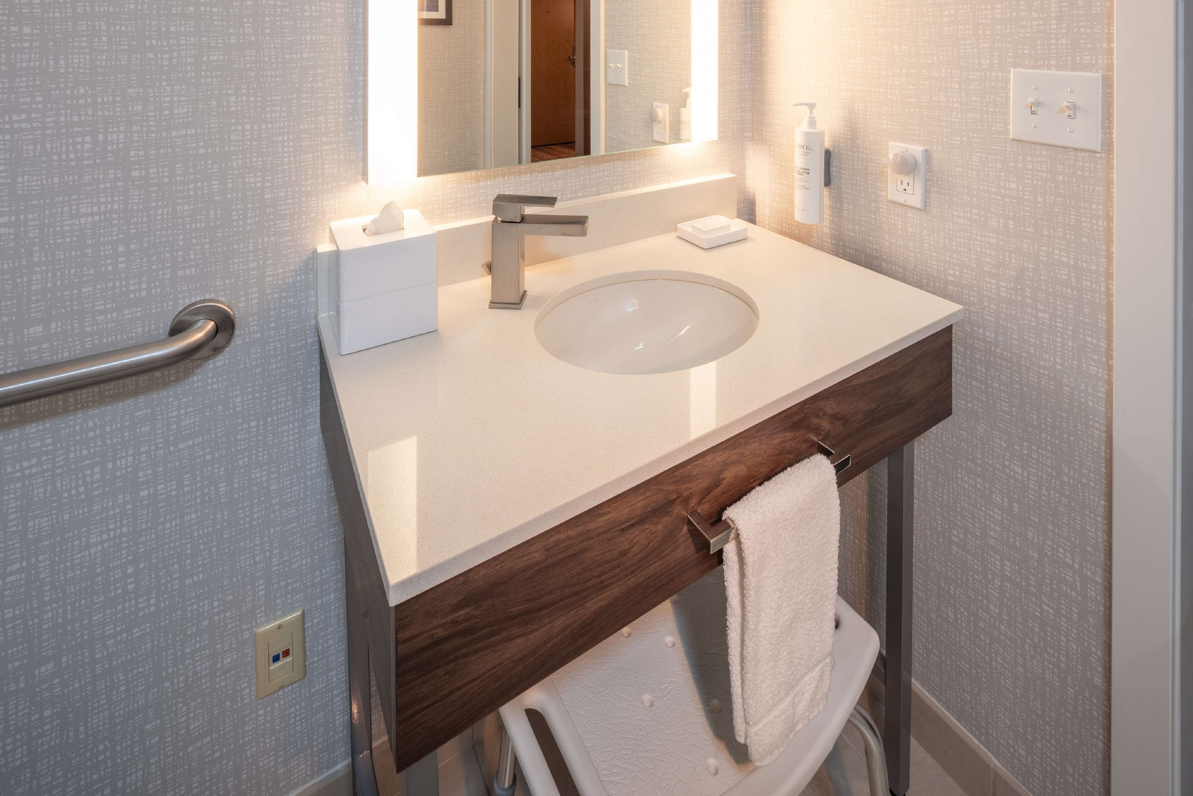 A modern bathroom with a white sink, a wooden vanity, a towel rack, and a mirror.