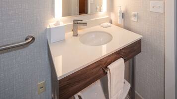 A modern bathroom with a white sink, a wooden vanity, a towel rack, and a mirror.