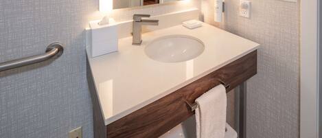 A modern bathroom with a white sink, a wooden vanity, a towel rack, and a mirror.