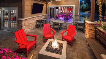 Un patio al aire libre con sillas rojas, un pozo de fuego y una zona de bar con asientos.