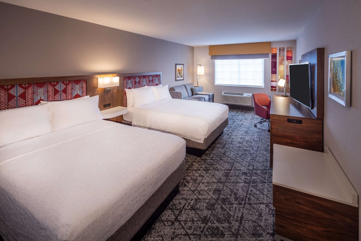 Quarto de hotel com duas camas, uma escrivaninha, uma televisão e uma janela.