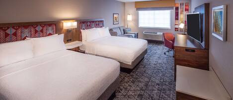 A hotel room with two beds, a desk, a TV, and a window.
