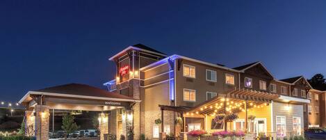 A hotel with a covered entrance, outdoor seating area, and a sign indicating 'Welcome'.
