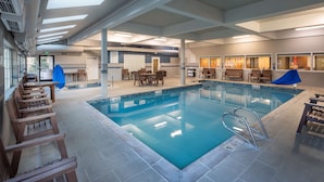 An indoor swimming pool with clear water, surrounded by wooden chairs and tables, and a covered seating area. - Hampton Inn Pullman (Pullman)