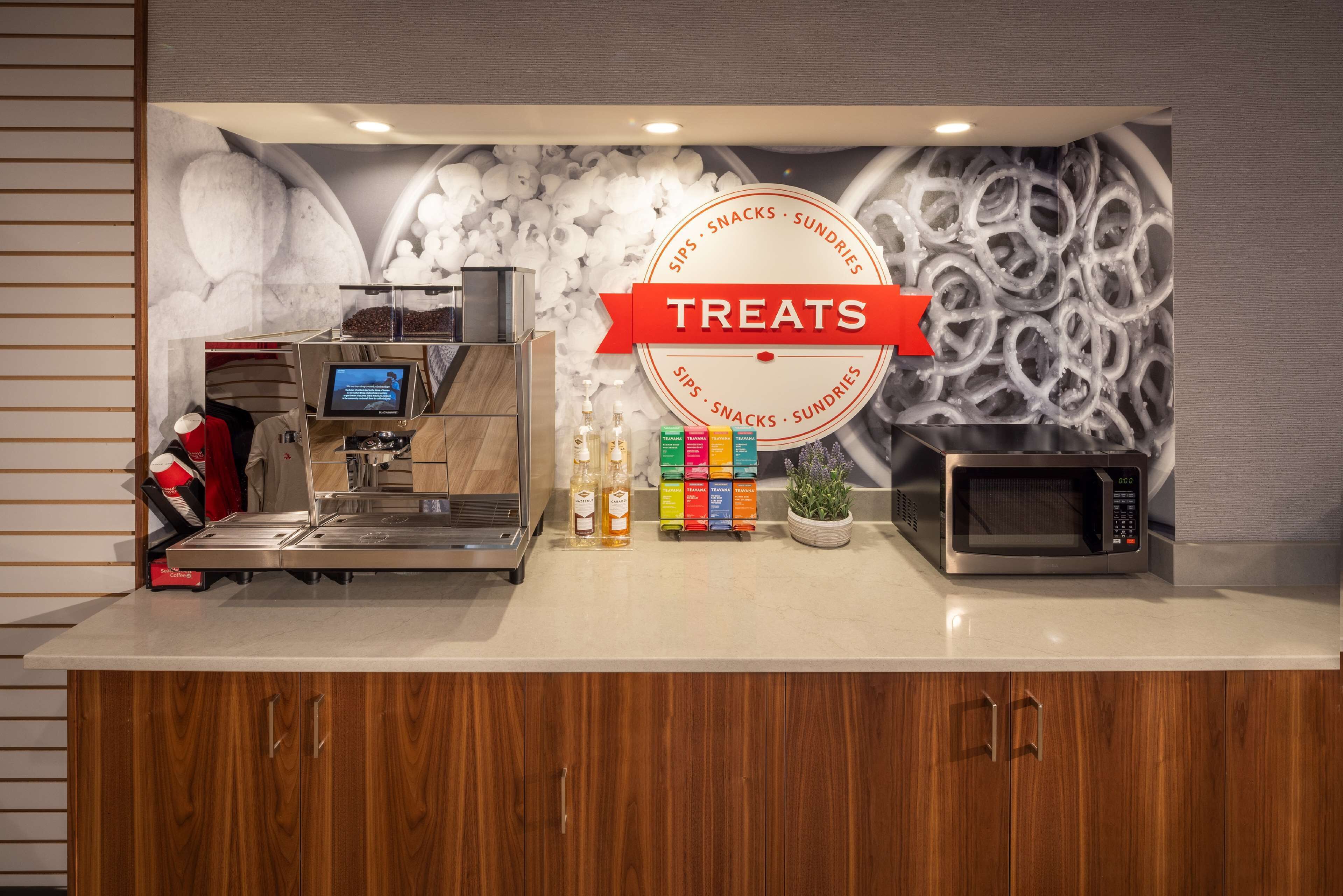 A modern kitchen area with a coffee machine, a microwave, and a display of colorful beverage bottles.