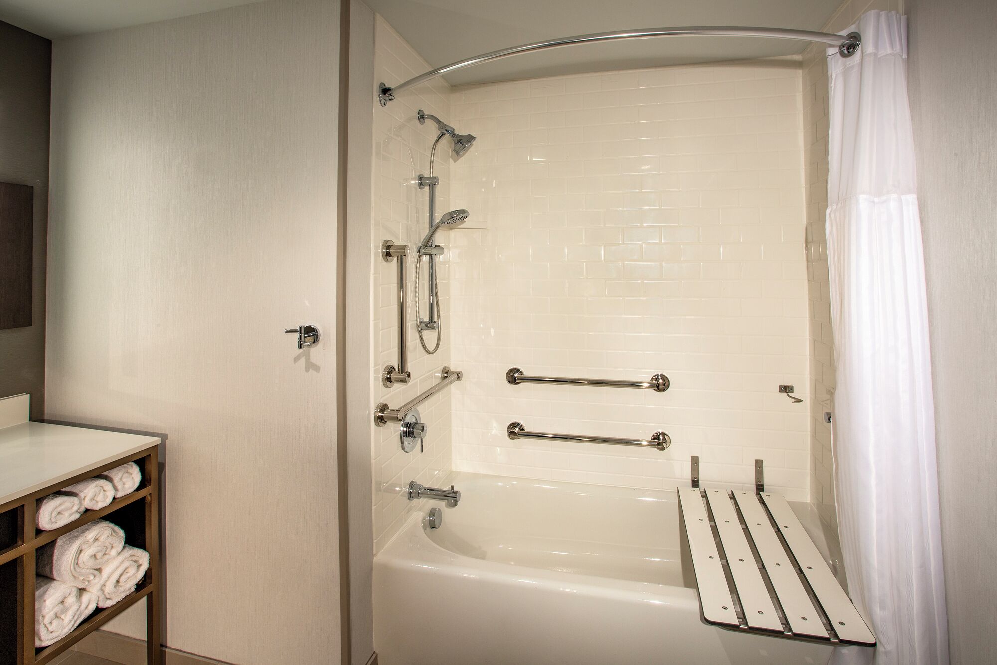 Een moderne badkamer met een badkuip, douche en handgrepen.