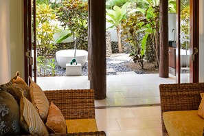 Una habitación con mobiliario de mimbre, una bañera blanca y vistas a un jardín.