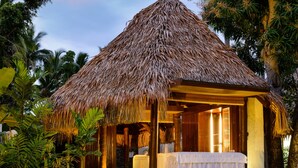 A thatched-roof hut with a bed and a small table, surrounded by tropical vegetation. - The Westin Fiji Golf Resort & Spa (Nadi)