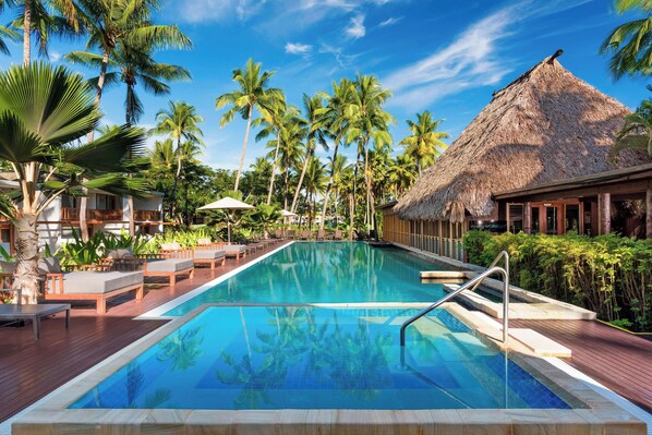 A swimming pool with lounge chairs and palm trees.