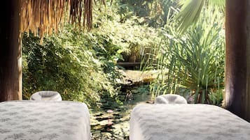 Guests can relax in a serene garden setting with two beds surrounded by lush greenery and a small pond.