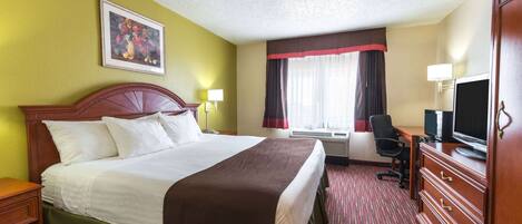 A hotel room with a large bed, a desk with a computer, a television, and a window with curtains.