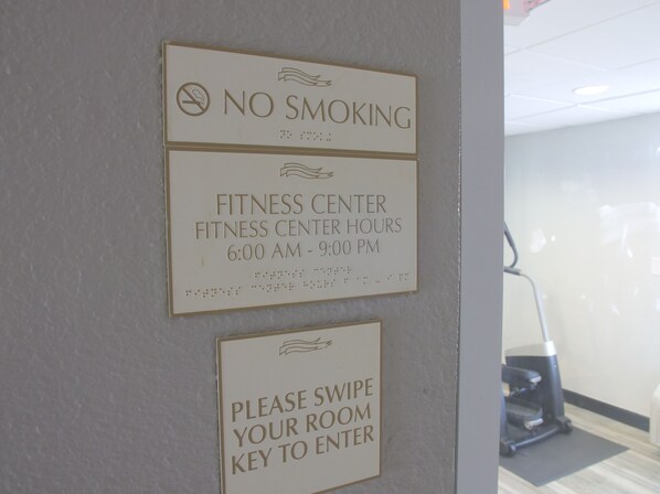 Una pared con carteles que indican prohibido fumar, horario del gimnasio y la solicitud de usar la llave de la habitación para entrar.