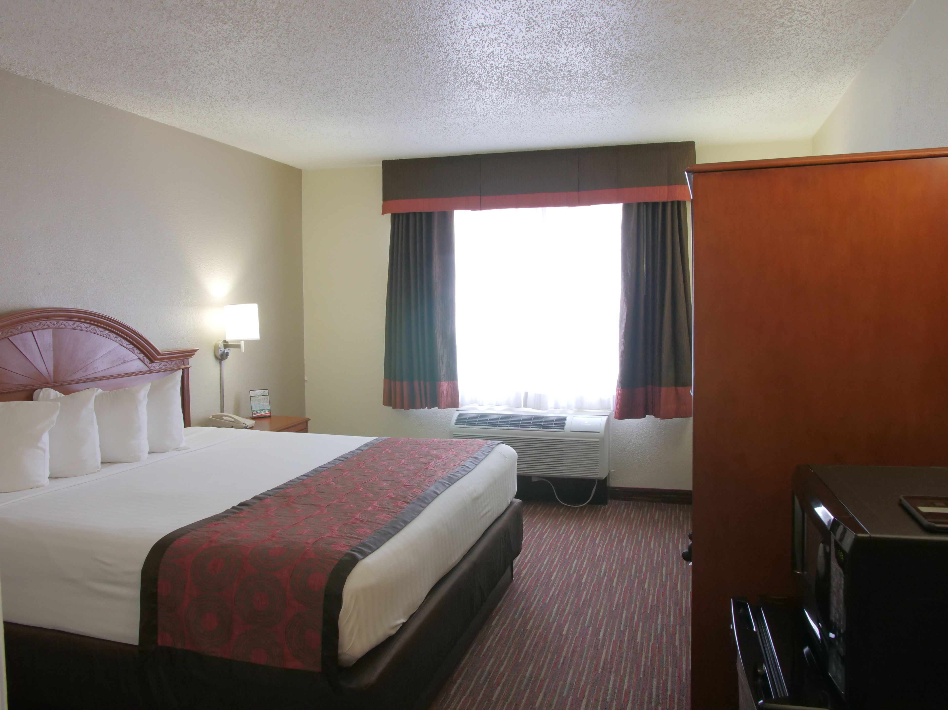 Habitación de hotel con una cama grande, un escritorio, una silla, un televisor y una ventana con cortinas.