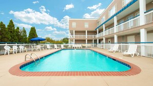 A swimming pool with a brick edge, surrounded by white lounge chairs and a building with balconies. - Baymont by Wyndham Louisville East (Louisville)