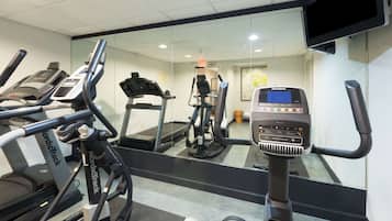 A gym with treadmills, an elliptical, and a stationary bike, featuring a large mirror and a mounted TV.