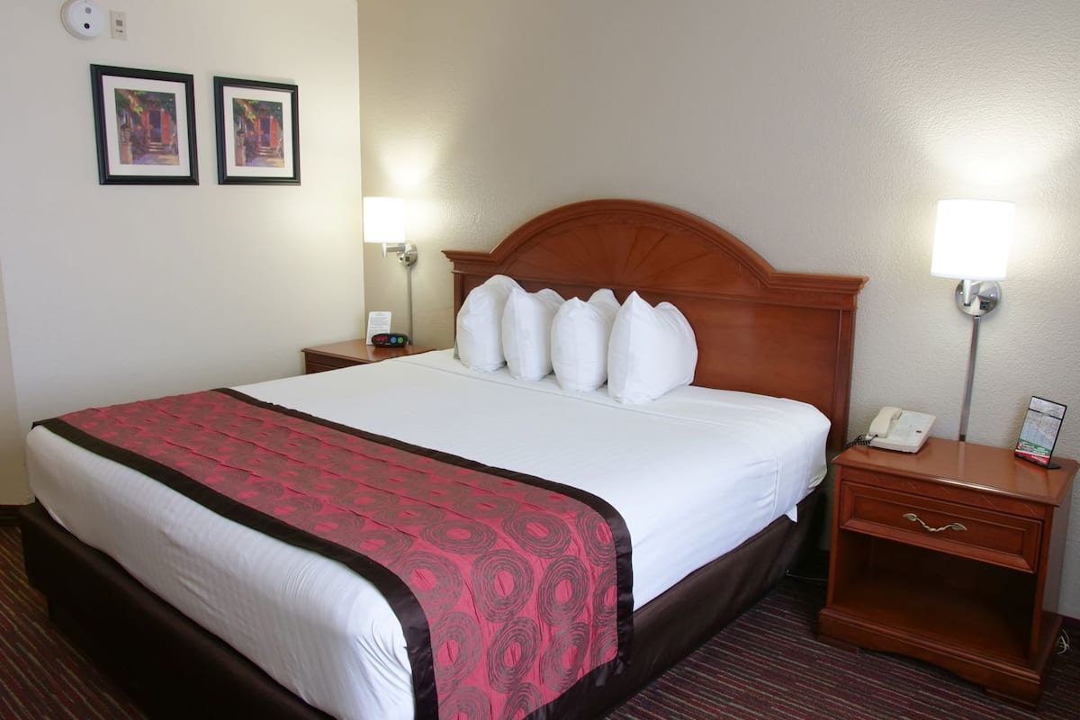 Une chambre d’hôtel avec un grand lit, deux tables de chevet, une tête de lit en bois et deux lampes fixées au mur.