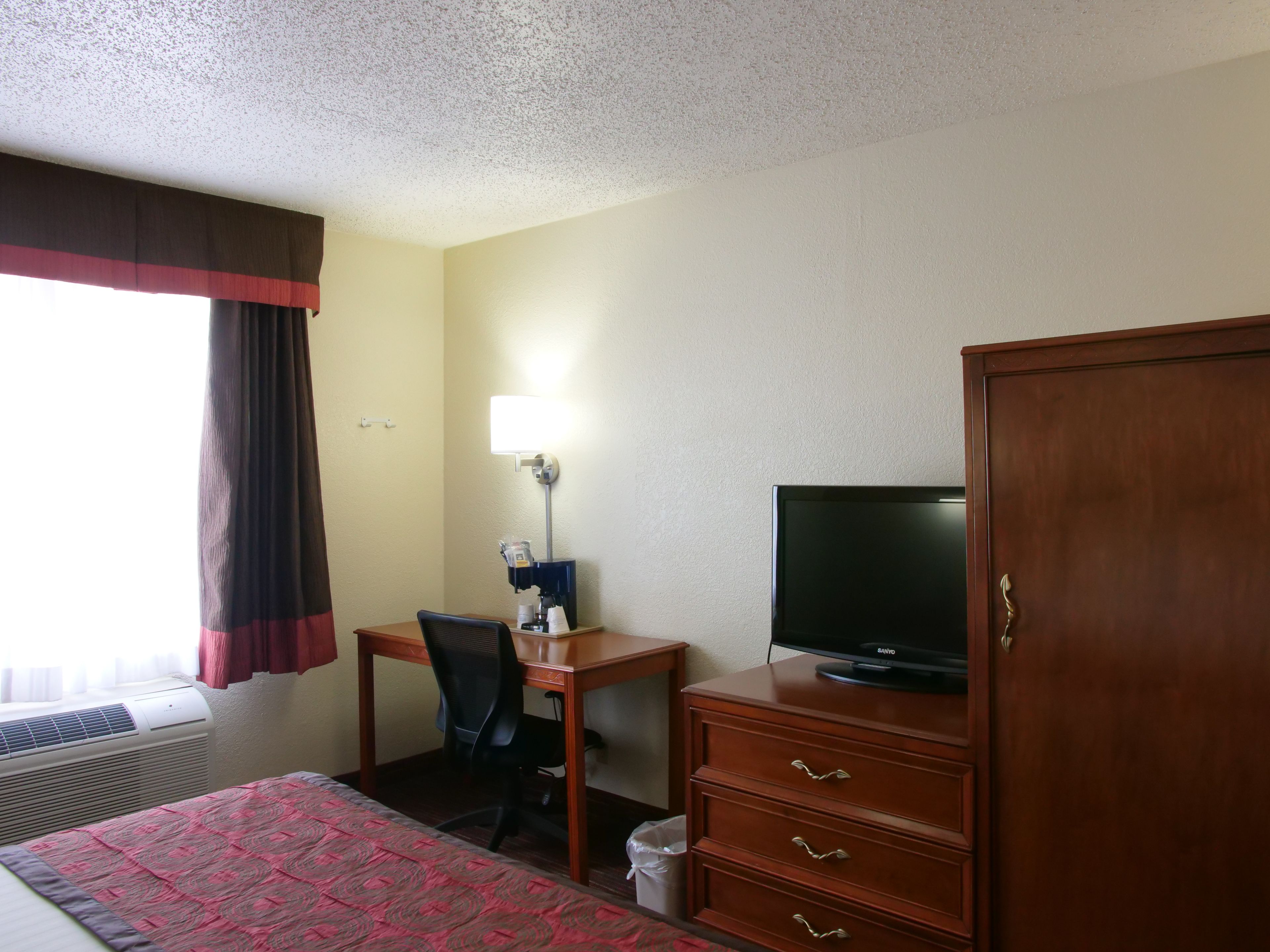 A hotel room with a bed, a desk with a chair, a television, and a wardrobe.