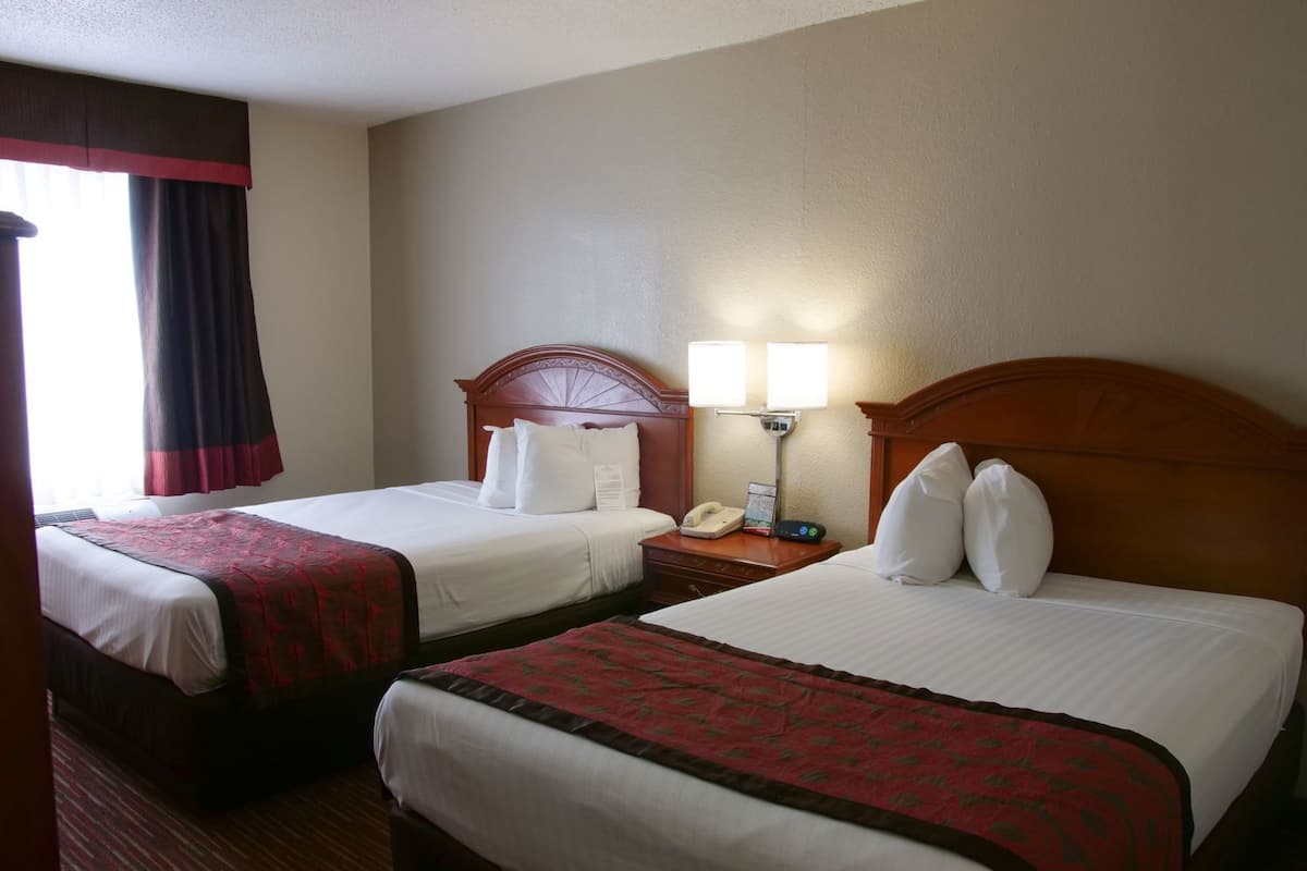 Une chambre d’hôtel avec deux lits, une table de chevet avec un téléphone et une lampe, et une fenêtre avec des rideaux.