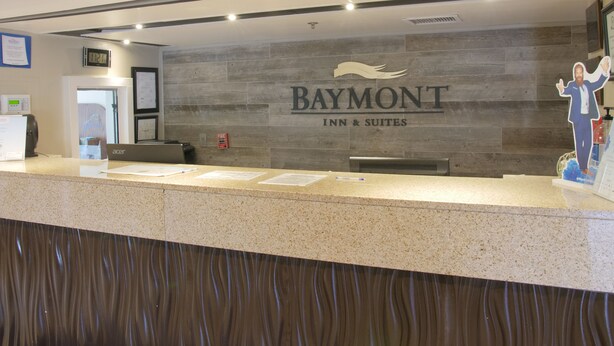 A reception desk with a sign for Baymont Inn & Suites, a fire alarm, and a clock. - Baymont by Wyndham Louisville East (Louisville)