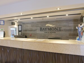 A reception desk with a sign for Baymont Inn & Suites, a fire alarm, and a clock. - Baymont by Wyndham Louisville East (Louisville)