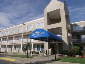Edifício do Baymont Inn & Suites com toldo azul, várias varandas e área de estacionamento com borda amarela.