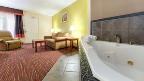 A hotel room with a large bathtub, a sofa, a chair, and a small table. - Baymont by Wyndham Louisville East (Louisville)