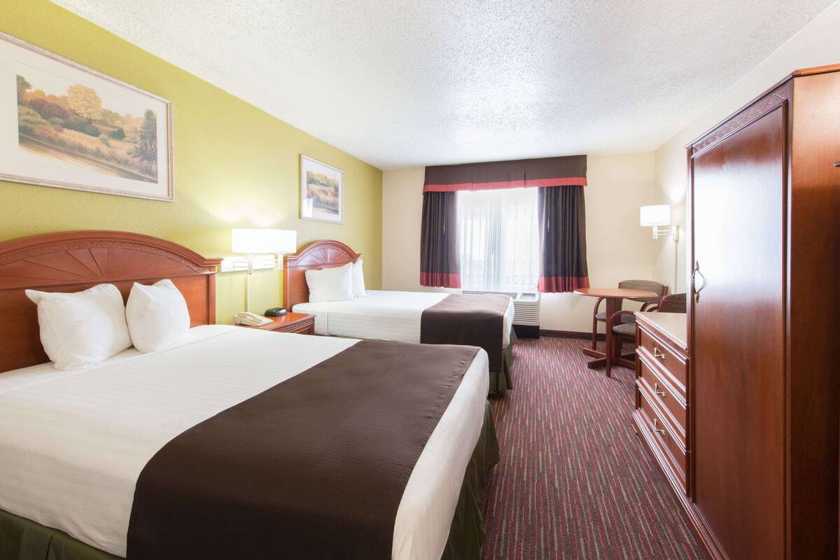 Une chambre d’hôtel avec deux lits, un bureau, une commode et un grand miroir.