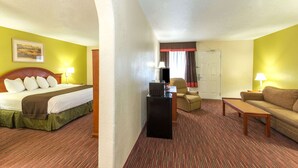 A hotel room with a bed, a desk, a chair, a sofa, and a door. - Baymont by Wyndham Louisville East (Louisville)
