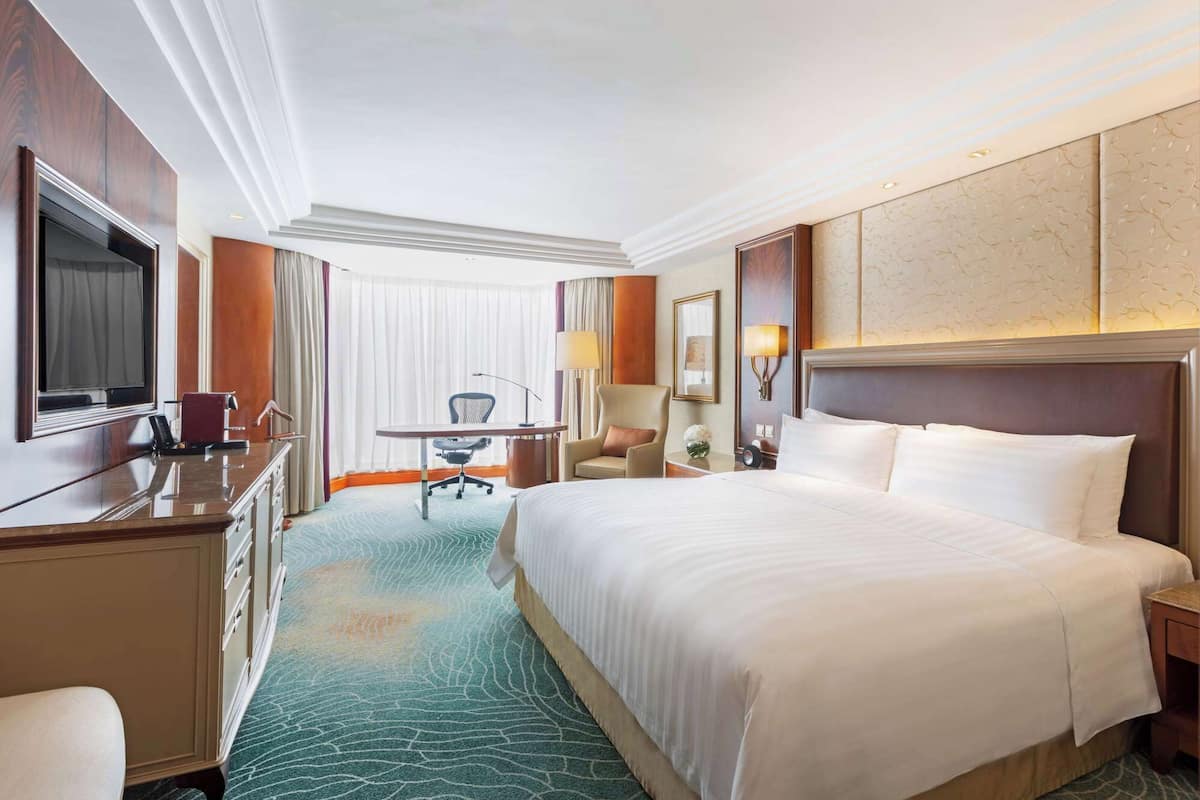 A hotel room with a large bed, a desk, a chair, a television, and a minibar.