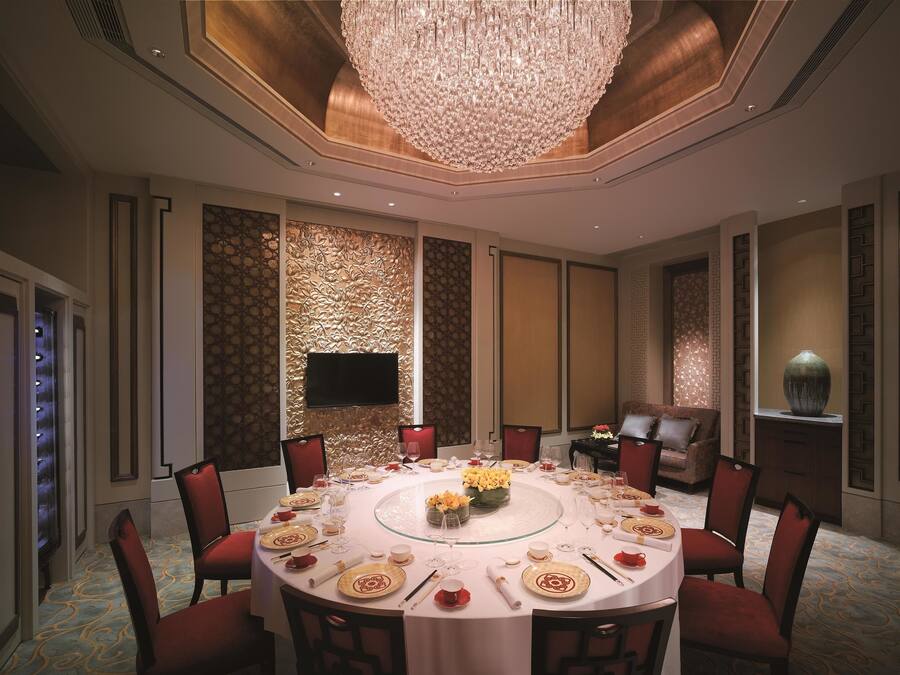 A formal dining room with a round table set for a meal, surrounded by red upholstered chairs.