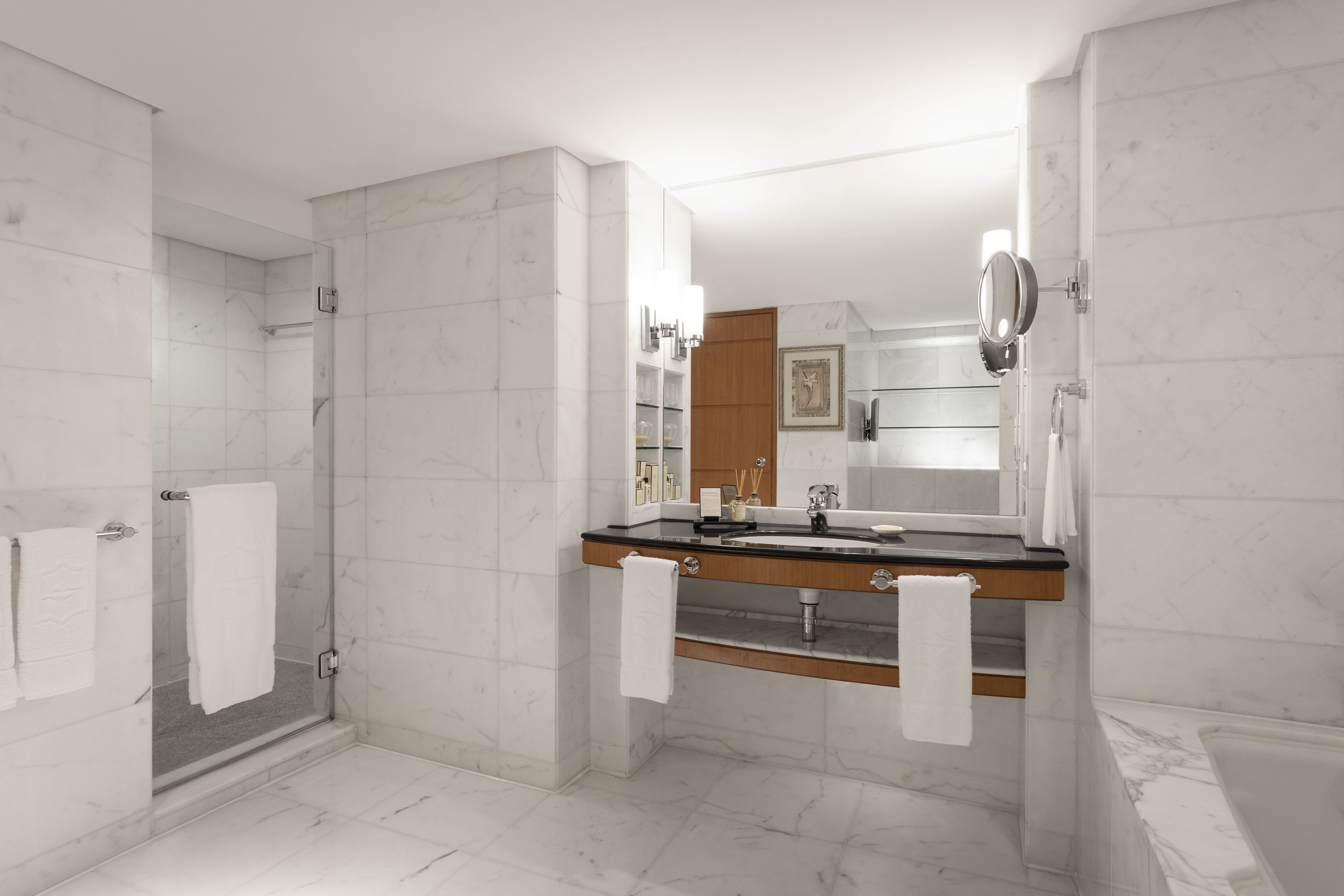 A modern bathroom with a glass-enclosed shower, a wooden vanity with a large mirror, and marble flooring.
