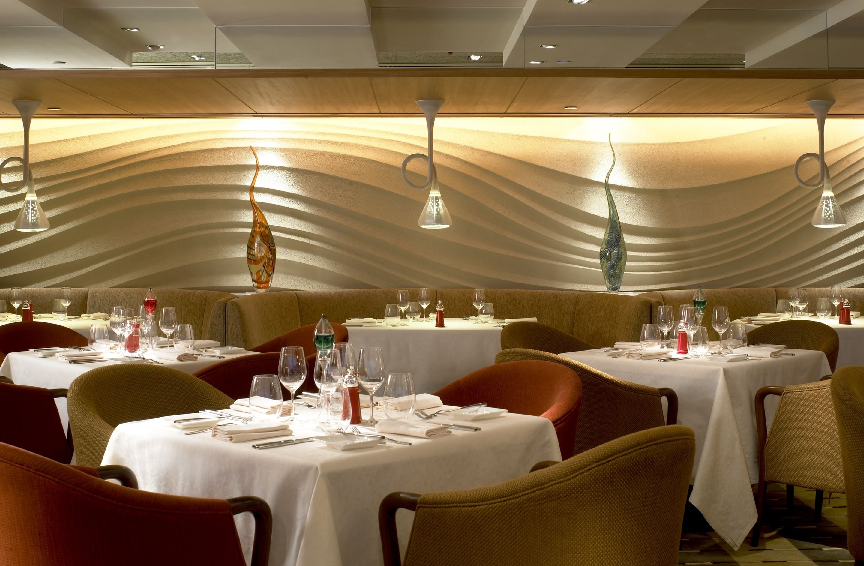 Een restaurant met gedekte tafels, met een opvallend golvend plafond en hanglampen.