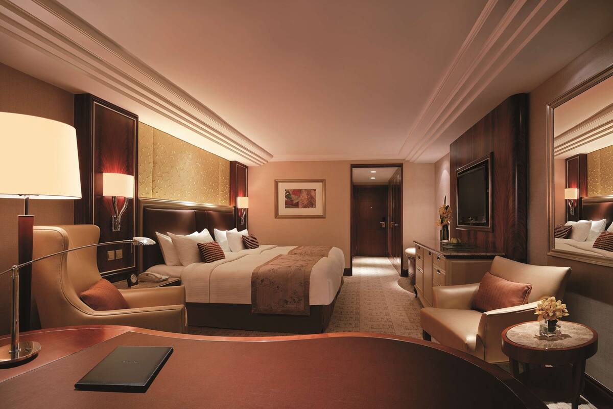 A hotel room with a bed, two chairs, a desk, a lamp, a TV, and a mirror.