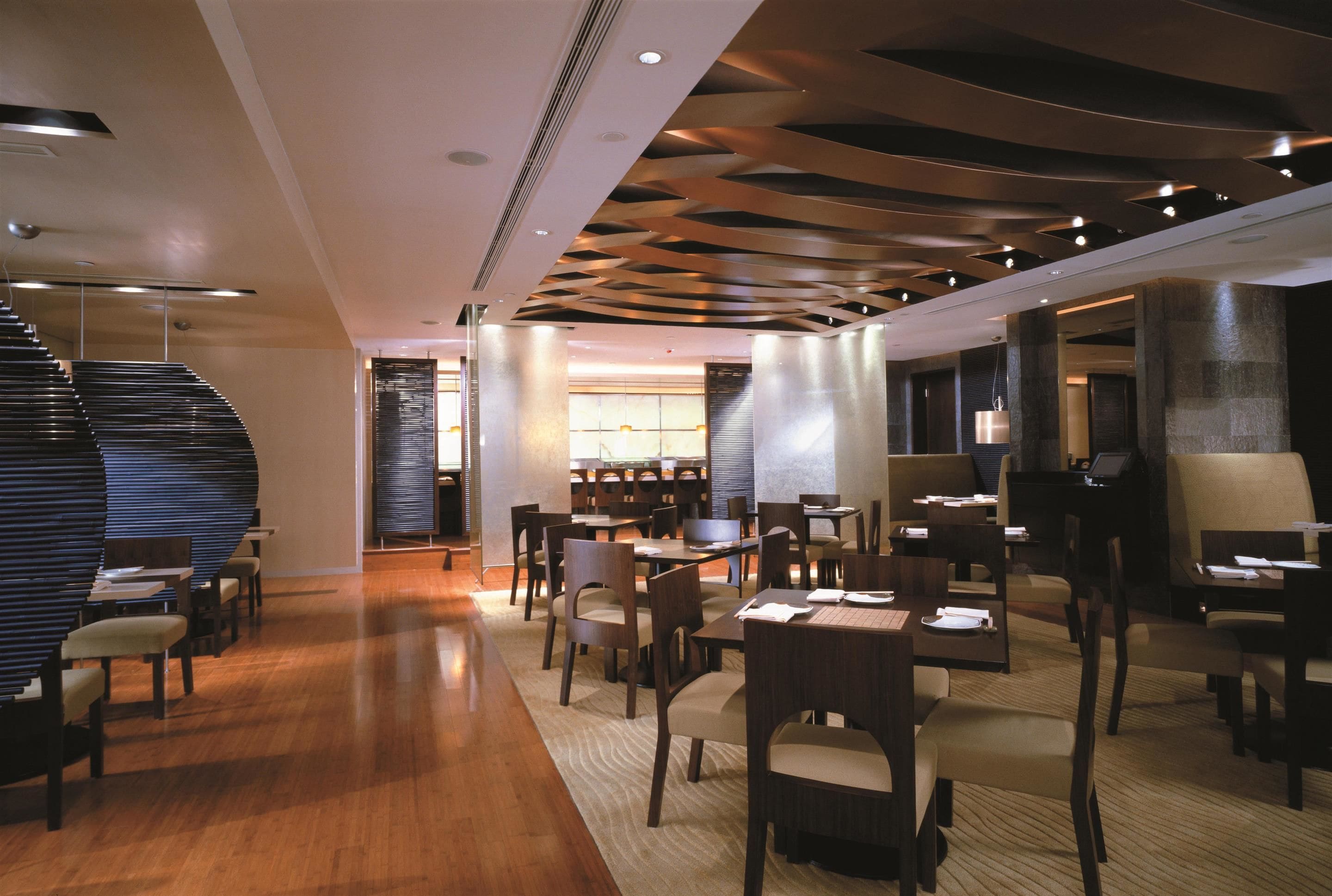 A modern hotel lobby with a wooden floor, a staircase, and a seating area with tables and chairs.
