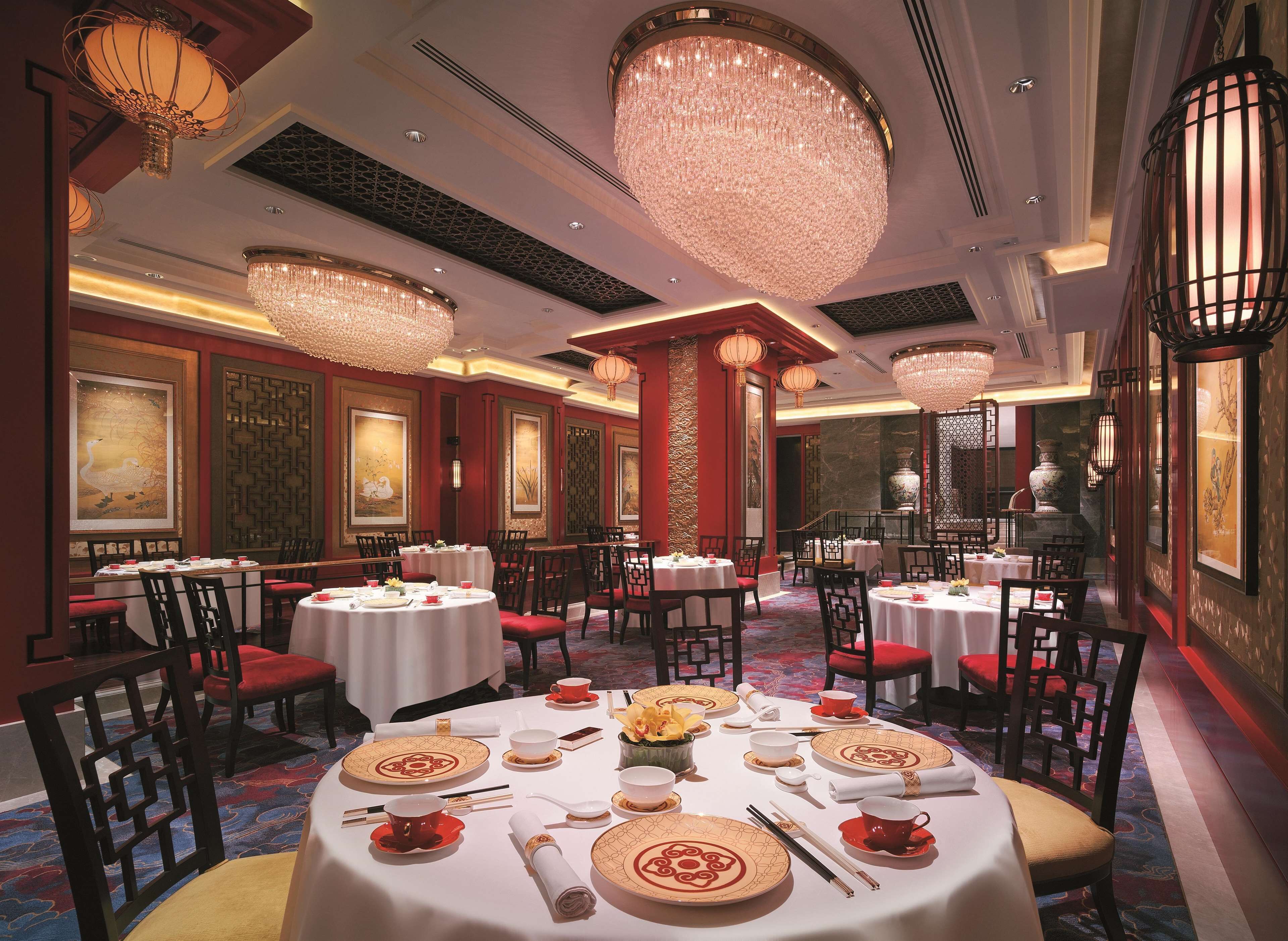 A formal dining room with round tables, red chairs, and traditional Chinese decor.