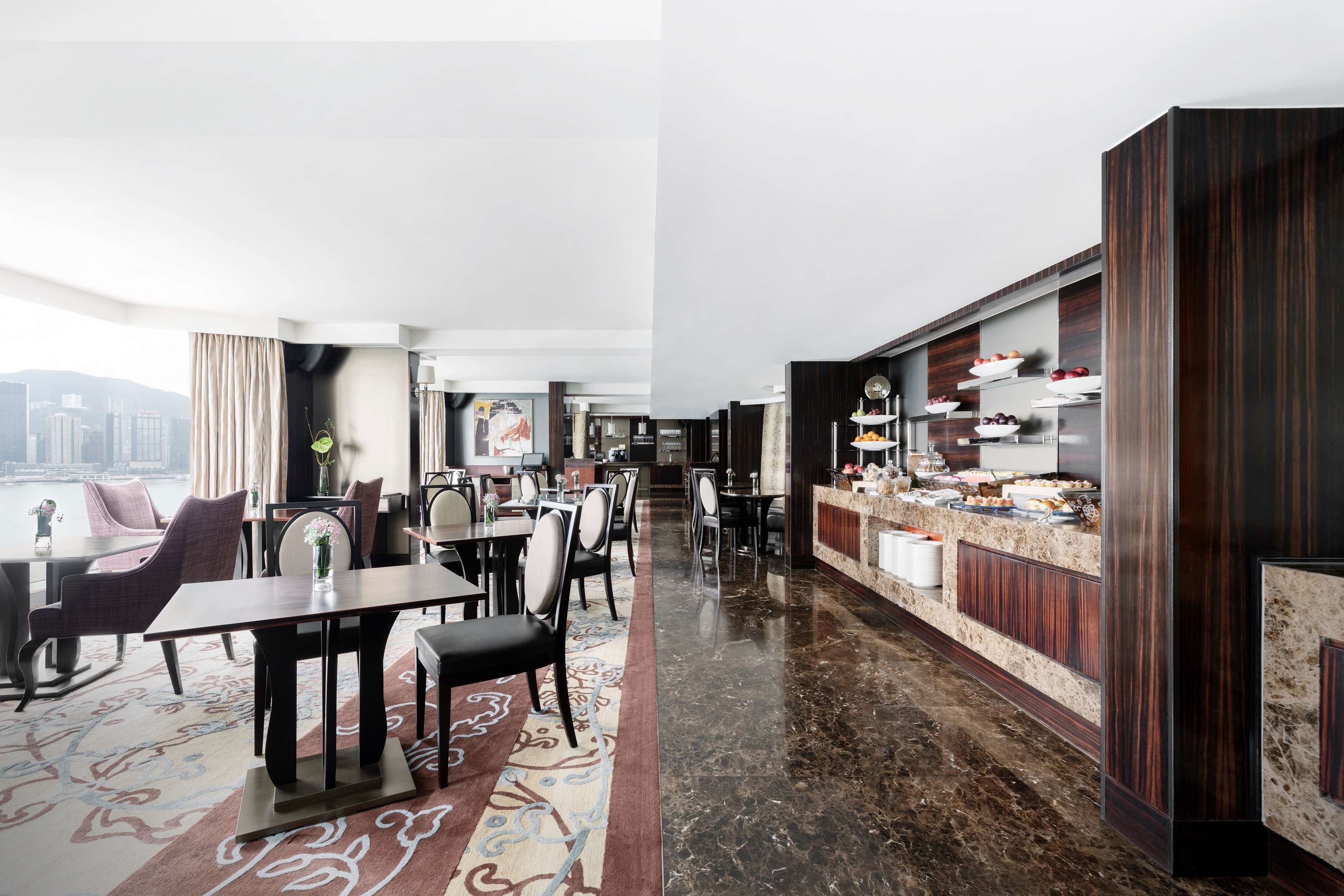 A modern hotel lobby with a dining area, a reception desk, and a view of the city.